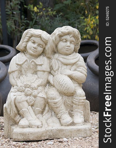 Concrete statue of boy with a rugby ball and girl with flowers sitting on a child bench. Concrete statue of boy with a rugby ball and girl with flowers sitting on a child bench.