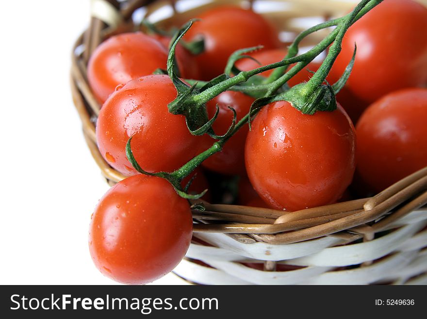 Red cherry tomatoes with a branch on a  wicker basket