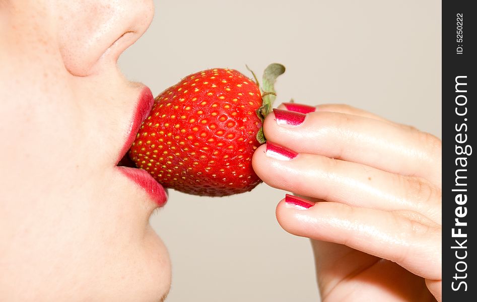 A girl, holding a strawberry between her red lips. A girl, holding a strawberry between her red lips