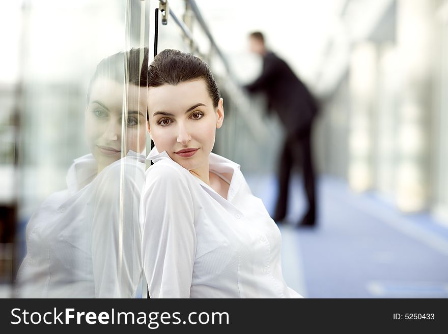 Portrait of young woman sitting on the floor in modern office building corridor and leaning against glass balustrade. Portrait of young woman sitting on the floor in modern office building corridor and leaning against glass balustrade