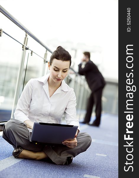 Portrait of young woman sitting with notebook on her lap in modern business office building corridor. Portrait of young woman sitting with notebook on her lap in modern business office building corridor