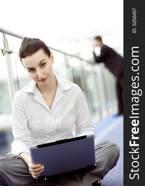 Portrait of young woman sitting with notebook on her lap in modern business office building corridor. Portrait of young woman sitting with notebook on her lap in modern business office building corridor
