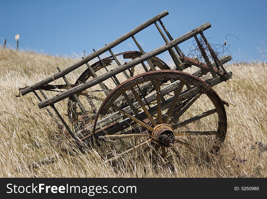Ancient abandoned chariot in a field in a summer day's blue sky with light clouds. Ancient abandoned chariot in a field in a summer day's blue sky with light clouds