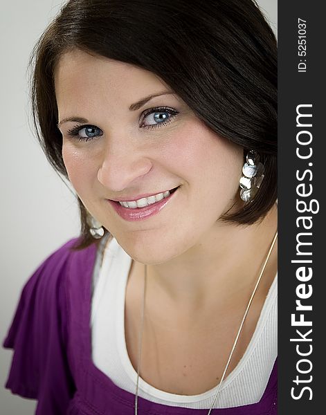 A blue-eyed and brunette Caucasian woman wearing a purple and a white shirt smiling. A blue-eyed and brunette Caucasian woman wearing a purple and a white shirt smiling