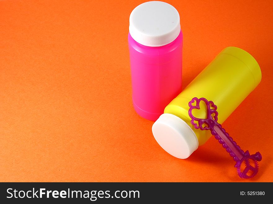 Two colorful bubble bottles and a blower, in orange background