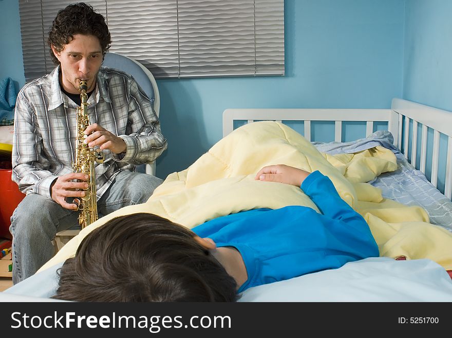 Young father playing a tune on a saxophone as his son gets ready to fall asleep. Young father playing a tune on a saxophone as his son gets ready to fall asleep