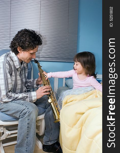 Little girl reaching out to grab her father's saxophone while he plays her a lullaby. Little girl reaching out to grab her father's saxophone while he plays her a lullaby