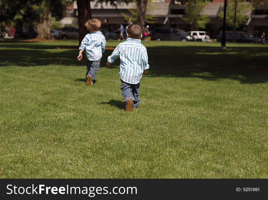 Outdoors shot of two young brothers running away from the camera, wearing identical button-up shirts and blue jeans. Outdoors shot of two young brothers running away from the camera, wearing identical button-up shirts and blue jeans.