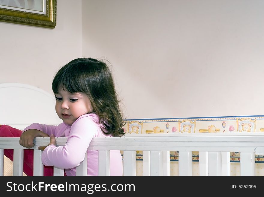 Adorable young girl climbing around the guardrail of a bedroom crib