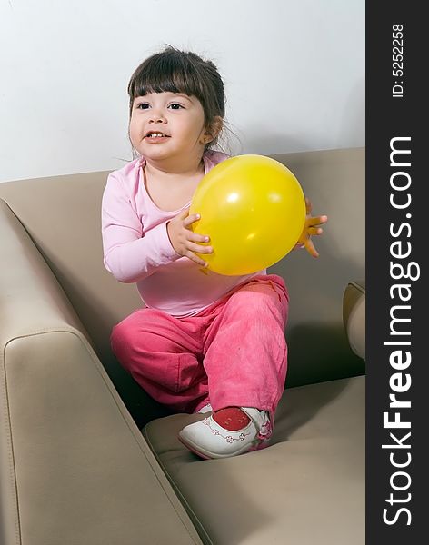 Cute young girl playing with a bright yellow balloon on a couch in her living room. Cute young girl playing with a bright yellow balloon on a couch in her living room