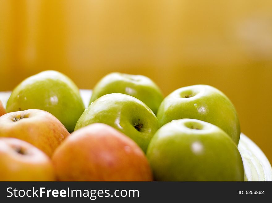 Green and red apples on plate on yellow background