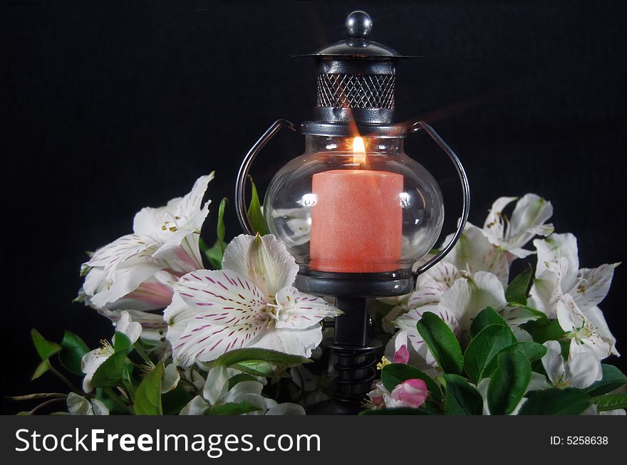 Glowing peach candle in pewter candle holder with lilies. Glowing peach candle in pewter candle holder with lilies.