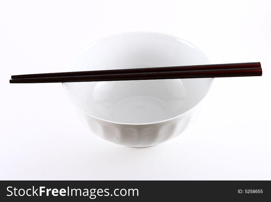 A pair of chopsticks placed on top of a white bowl isolated on white. A pair of chopsticks placed on top of a white bowl isolated on white.