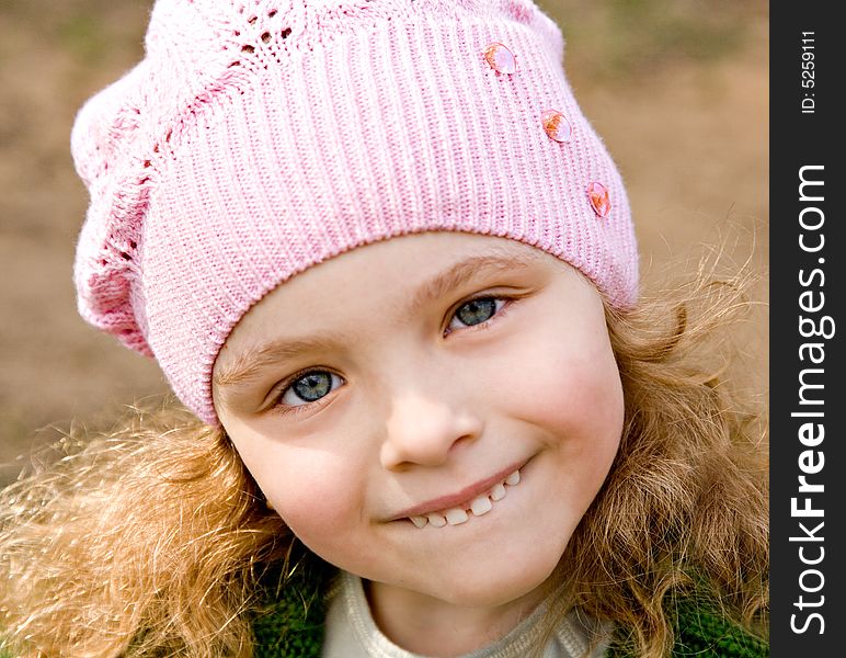 Portrait of the cheerful little girl in a pink cap with long hair