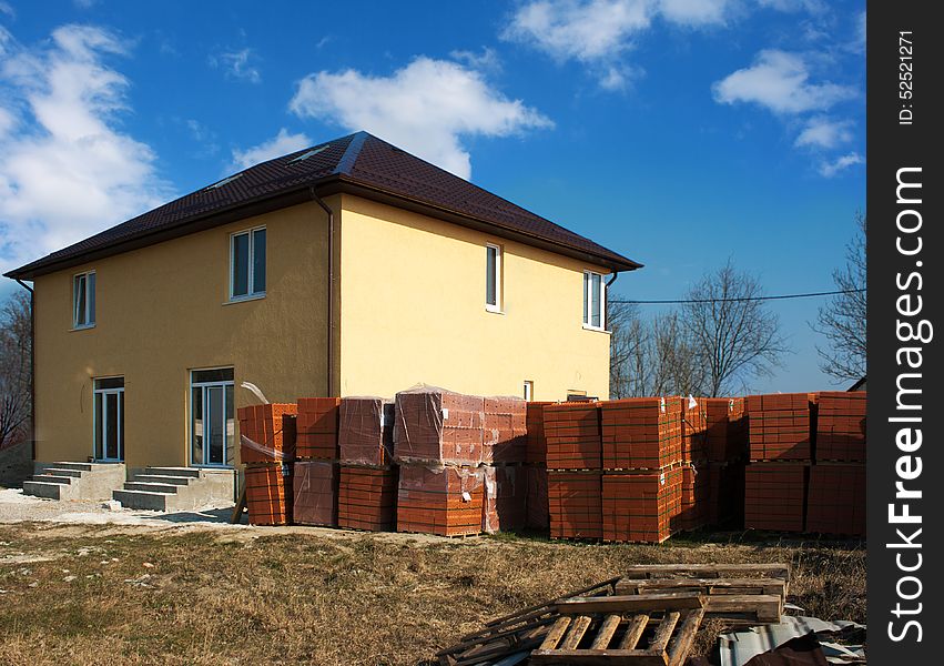 New yellow house with stacks of red bricks for the construction on sunny spring day. New yellow house with stacks of red bricks for the construction on sunny spring day