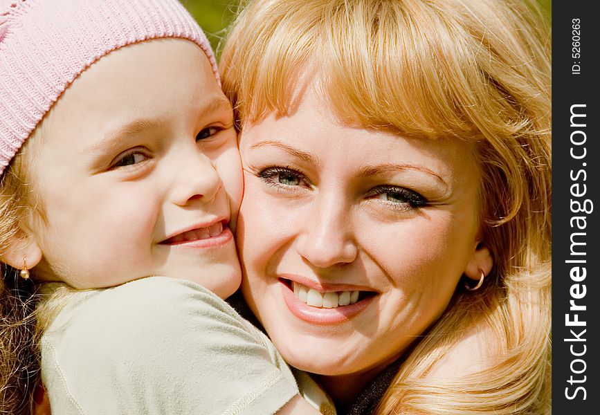 The beautiful little girl in a pink cap embraces mum with light hair. The beautiful little girl in a pink cap embraces mum with light hair