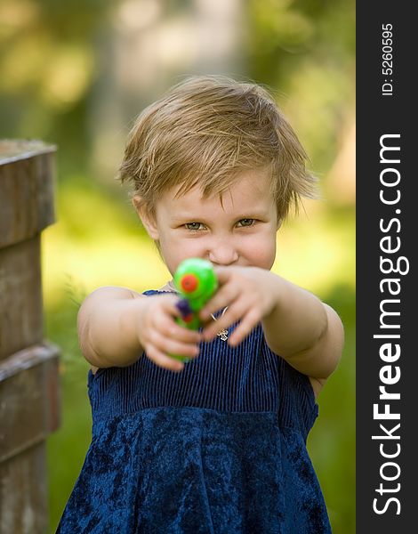 The little girl in a dark blue dress is going to shoot from a water pistol in summer day