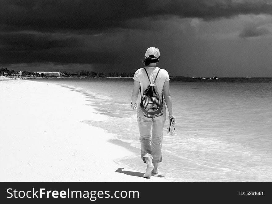 The girl walking on Our Lucaya beach with stormy dark clouds in a background on Grand Bahama Island, The Bahamas. The girl walking on Our Lucaya beach with stormy dark clouds in a background on Grand Bahama Island, The Bahamas.