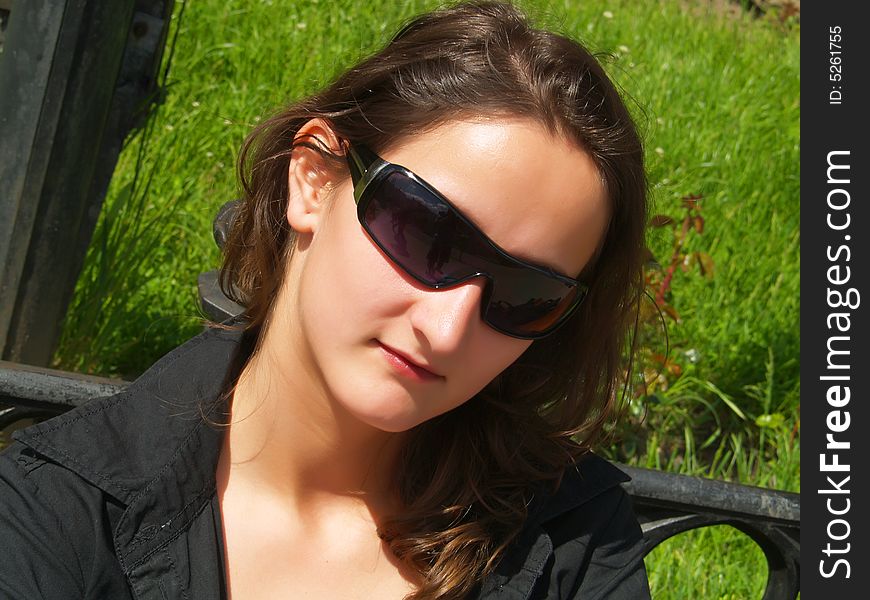 A portrait about an attractive trendy girl with brown hair who is sitting on a bench in downtown and she is wearing sunglasses and a black shirt. A portrait about an attractive trendy girl with brown hair who is sitting on a bench in downtown and she is wearing sunglasses and a black shirt.