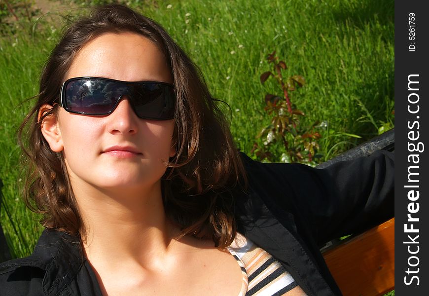 A portrait about an attractive trendy girl with brown hair who is sitting on a bench in downtown and she is wearing sunglasses and a black shirt. A portrait about an attractive trendy girl with brown hair who is sitting on a bench in downtown and she is wearing sunglasses and a black shirt.