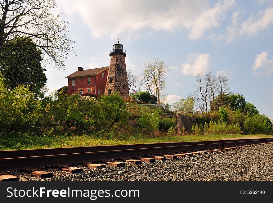 A landscape view of a vintage lighthouse on a hill by train tracks,. A landscape view of a vintage lighthouse on a hill by train tracks,