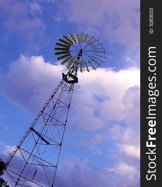 A tall wind-mill in the park, with a background of beautiful clouds in the sky