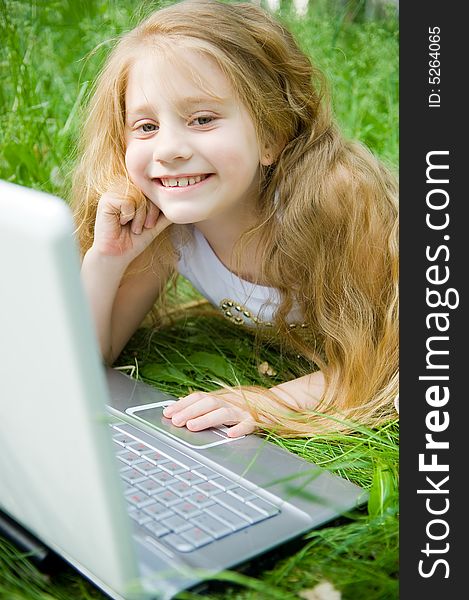 Smiling little girl with laptop in green grass