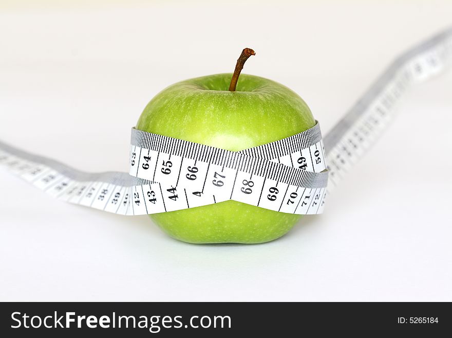 An green apple with a measuring tape around it on a white background. An green apple with a measuring tape around it on a white background.