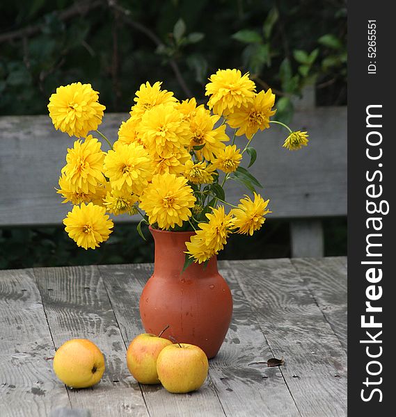 Yellow flowers in a clay jug with yellow apples