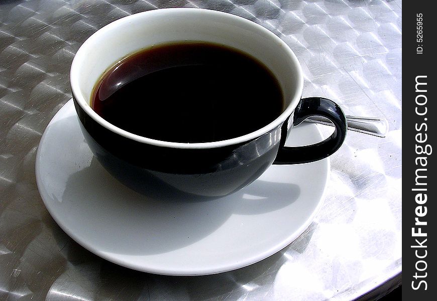 Coffee cup and saucer with spoon on metal table