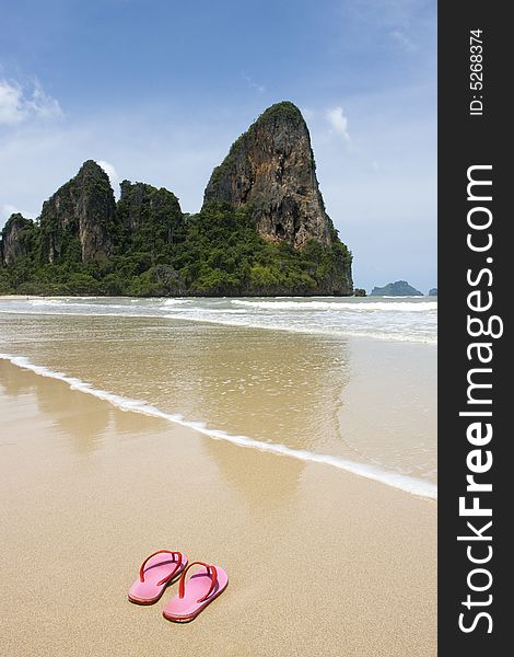 Colorful pink flip flops on beach in Thailand, limestone rock in background