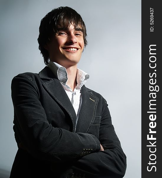 A portrait about a trendy attractive young man who is smiling and he has charming look. He is wearing a white shirt and a stylish black suit.