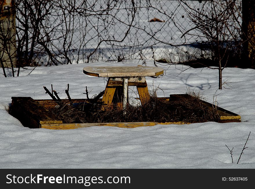 Abandoned children's sandpit with a table in the snow.
Painted in yellow.