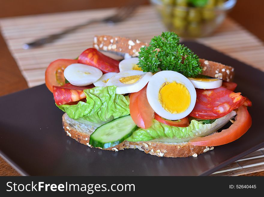 Fresh and tasty sandwich with salami and vegetables on a brown plate on a table. Fresh and tasty sandwich with salami and vegetables on a brown plate on a table