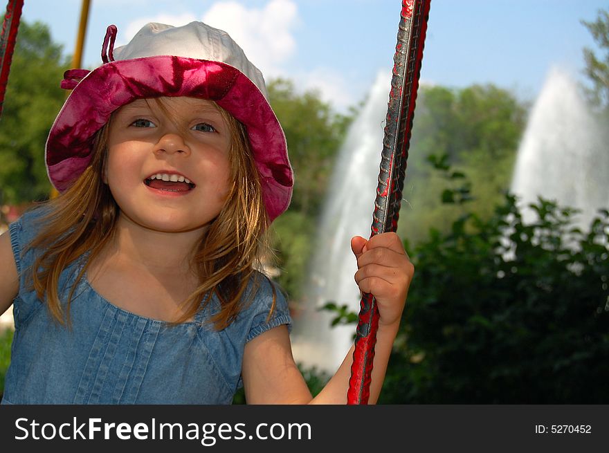 Little pretty swinging girl on the background of blue sky, trees and fountain. Little pretty swinging girl on the background of blue sky, trees and fountain