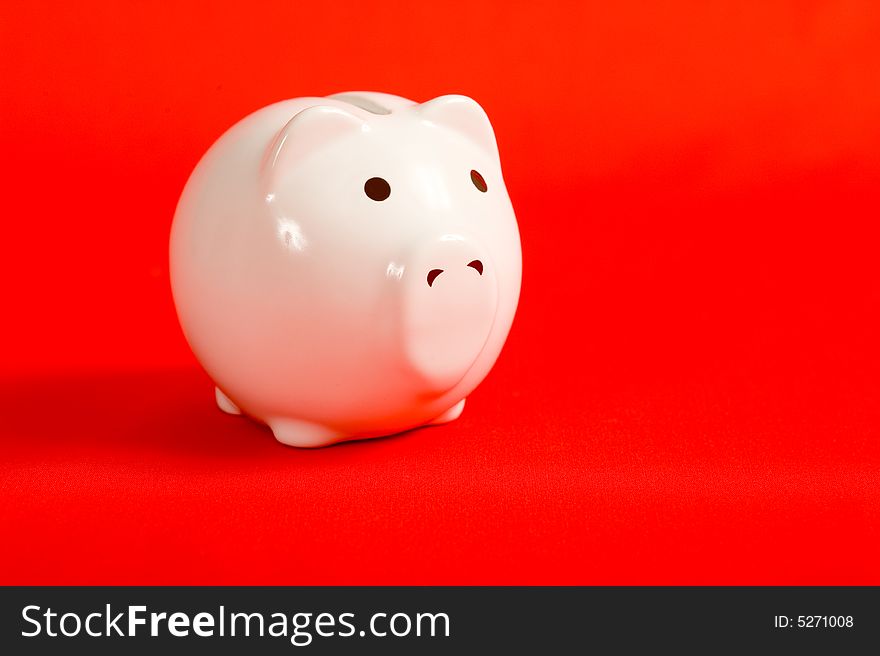 A white porcelain piggy bank on a red background with copy space. A white porcelain piggy bank on a red background with copy space