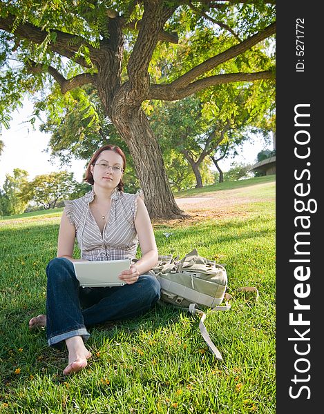 Female university student working on a laptop in green park