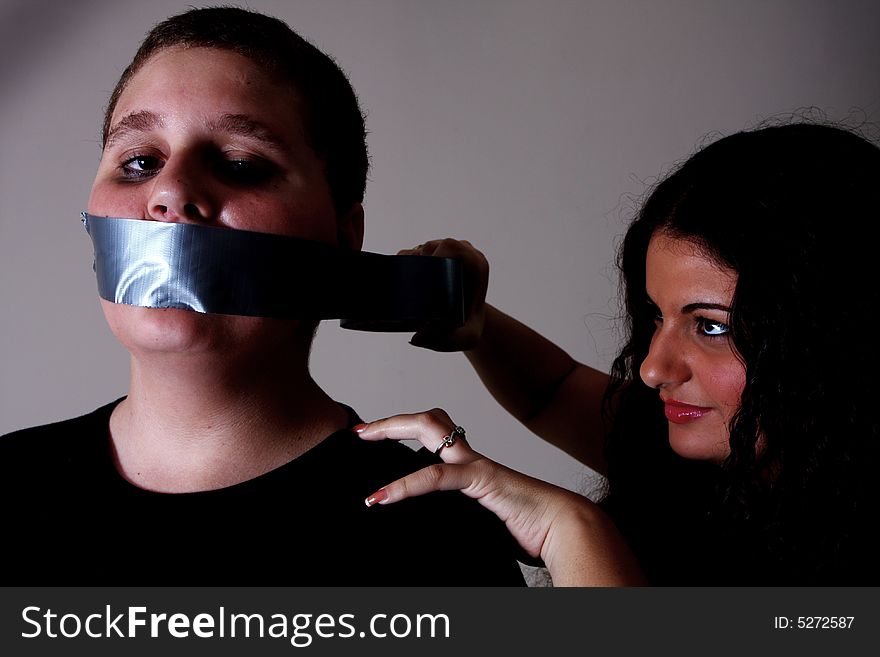 Woman taping a mans mouth with duct tape.