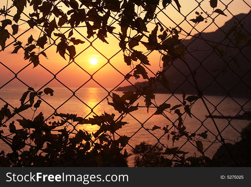 A sunset on the sea and a mountain behind the grid. A sunset on the sea and a mountain behind the grid