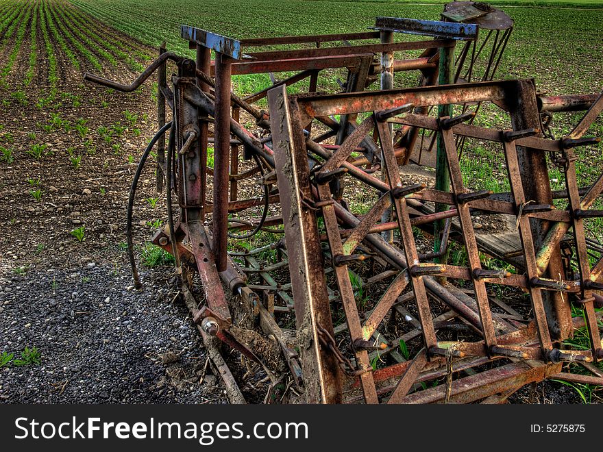 An old rusty farm machine in front of a grain field in HDR