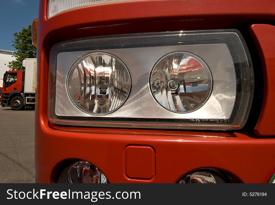 The headlamp of truck and in the background another truck. The headlamp of truck and in the background another truck