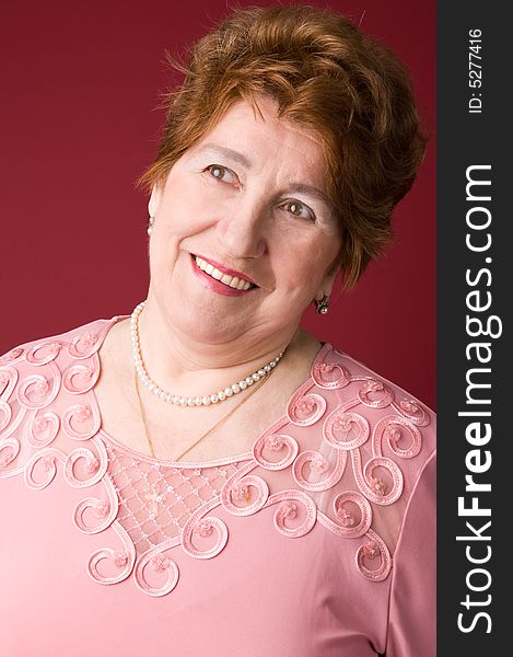 The cheerful elderly woman in a pink dress on a red background. The cheerful elderly woman in a pink dress on a red background.