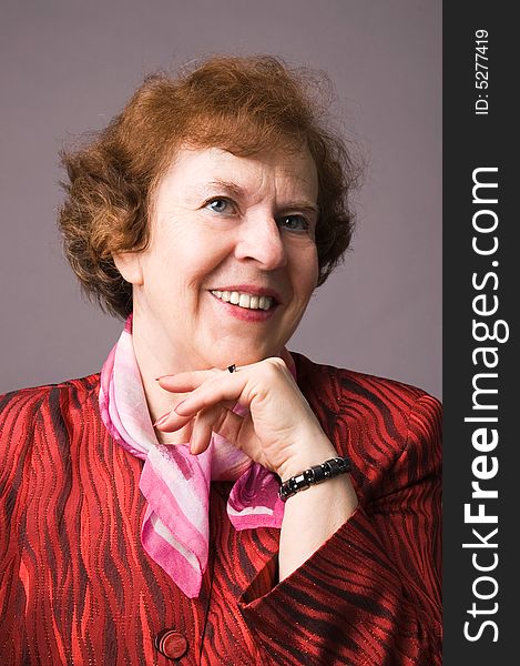 The cheerful elderly woman in a red dress on a grey background. The cheerful elderly woman in a red dress on a grey background.