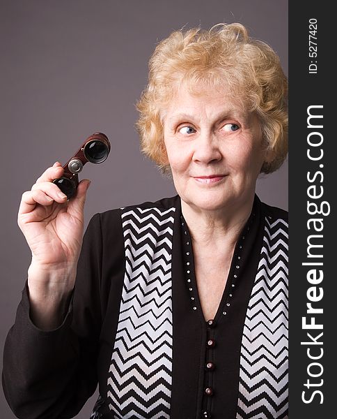 The cheerful elderly woman with binocular on a grey background. The cheerful elderly woman with binocular on a grey background.