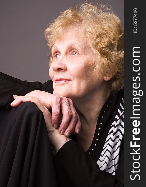 The elderly woman in a black dress on a grey background. The elderly woman in a black dress on a grey background.