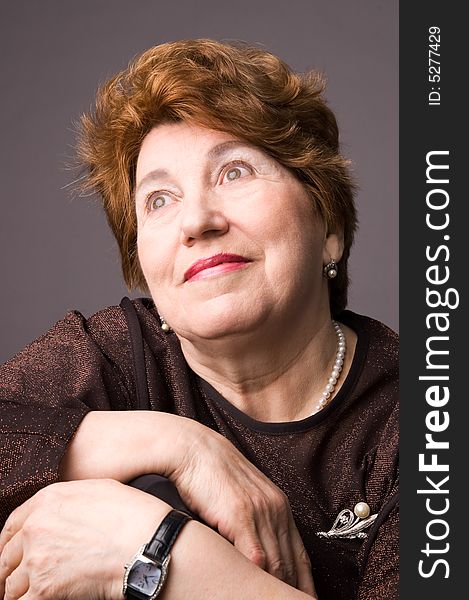 The cheerful elderly woman in a brown dress on a grey background. The cheerful elderly woman in a brown dress on a grey background.