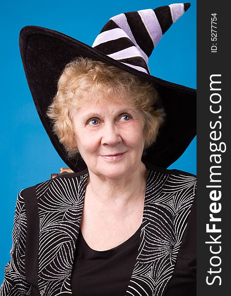 The cheerful elderly woman in witch's hat on a blue background. The cheerful elderly woman in witch's hat on a blue background.