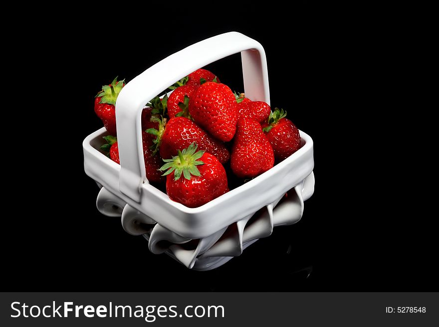 A white bowl of strawberries on black.