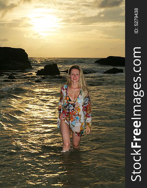 Young blonde woman walking in water of an ocean at sunset time.