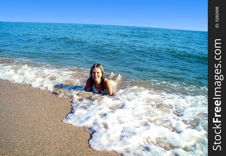 The lying girl on sand enjoys waves of a surf in the sea. The lying girl on sand enjoys waves of a surf in the sea.